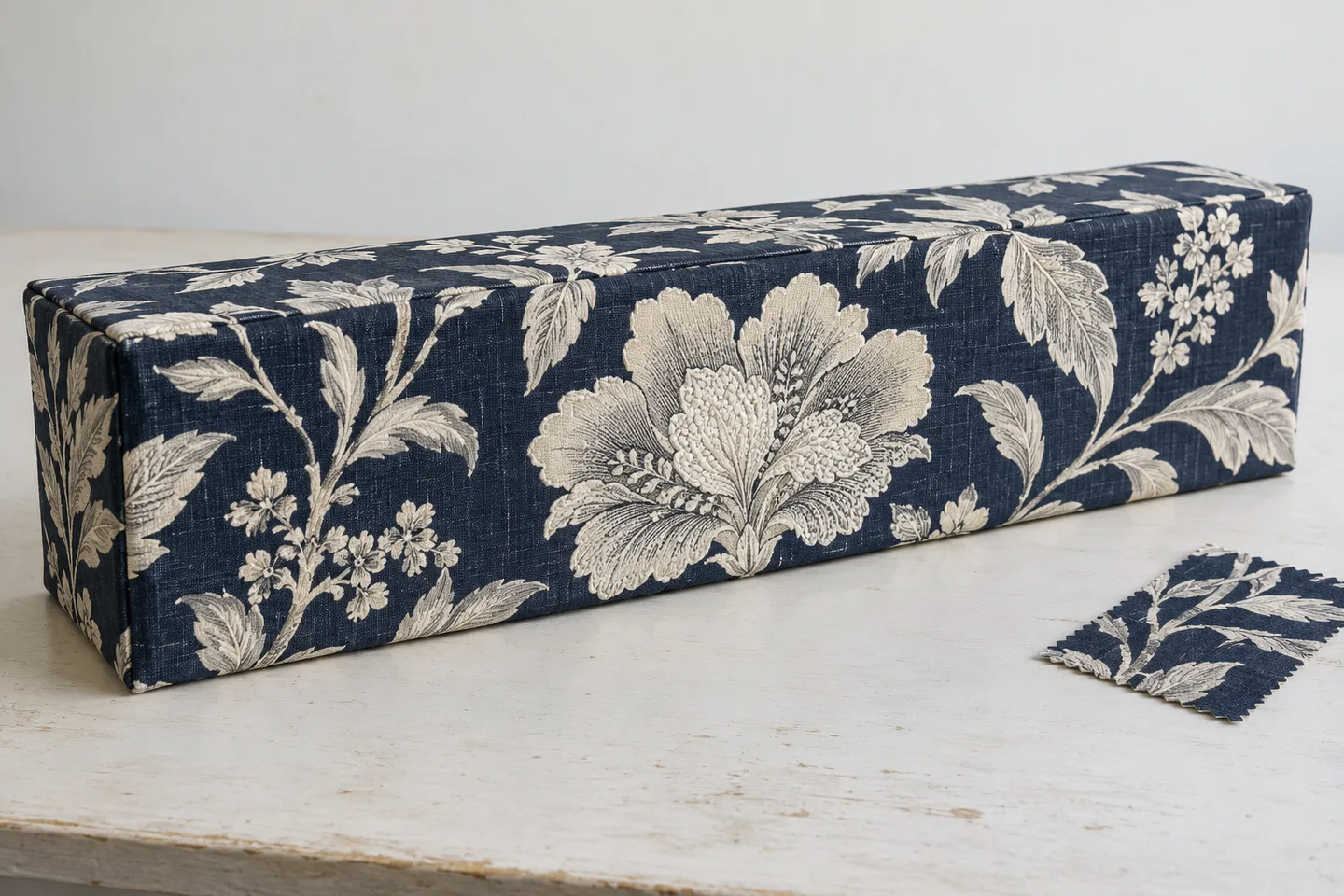 Navy and ivory botanical fabric covering a rectangular cornice with a centered front motif
