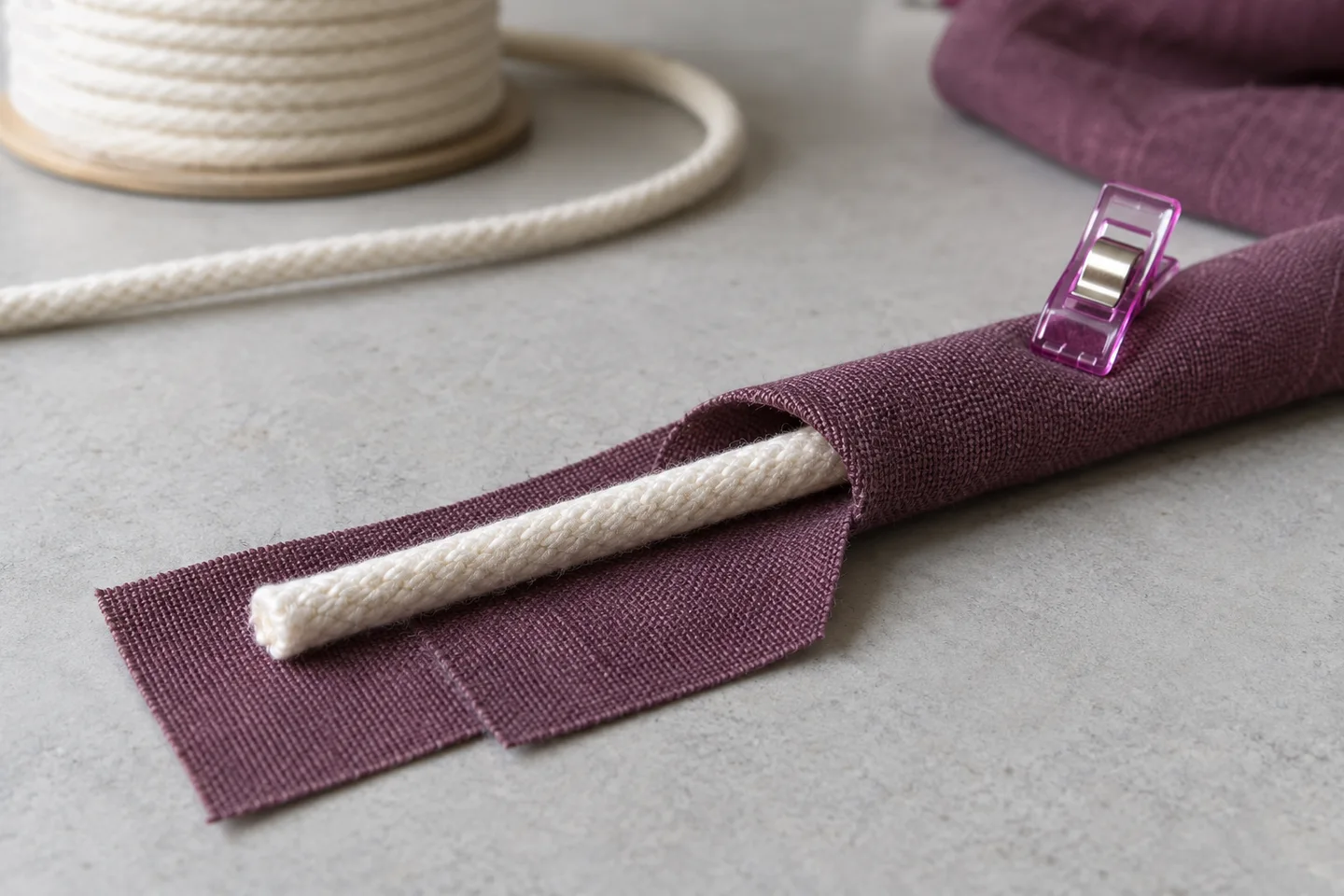 Plum fabric opened around cream piping cord with the folded seam flanges held by a sewing clip